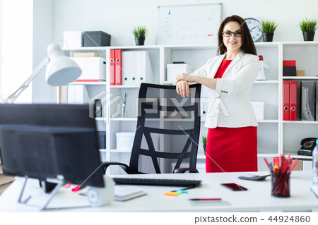 A young girl stands in the office near a chair in a high back. A young girl stands in the office near a chair in a high back. 44924860