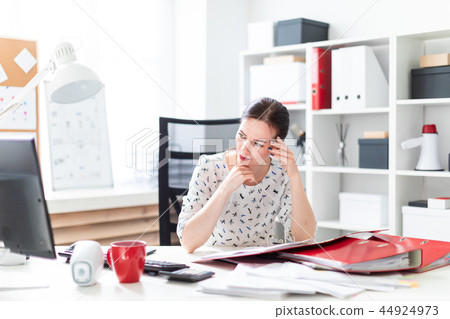 A young girl sitting in the office at the computer Desk, working with documents and holding hands on A young girl sitting in the office at the computer Desk, working with documents and holding hands on 44924973