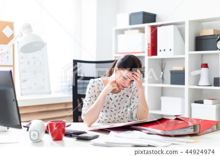 A young girl sitting in the office at the computer Desk, working with documents and holding hands on A young girl sitting in the office at the computer Desk, working with documents and holding hands on 44924974