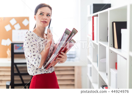 A young girl standing in the office, talking on the phone and holding a folder with documents. A young girl standing in the office, talking on the phone and holding a folder with documents. 44924976
