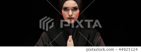 Portrait of beautiful serious young muslim woman wearing black hijab with hands near her face as 44925124