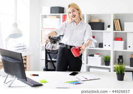 A young girl standing in the office and holding a Cup and a coffee pot. A young girl standing in the office and holding a Cup and a coffee pot. 44926657