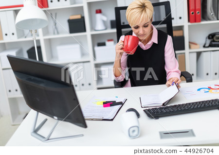 Girl sitting in the office at the table and drinking coffee. Girl sitting in the office at the table and drinking coffee. 44926704