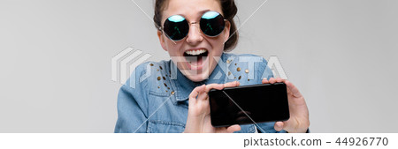 Young brunette girl in round glasses. Hairs are gathered in a bun. Girl with a black phone. 44926770