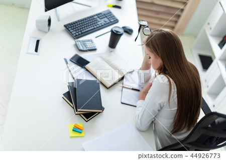 A young girl holding glasses and working in the office with books and documents. A young girl holding glasses and working in the office with books and documents. 44926773