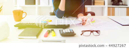 A young girl sits in the office at the table, holds a pen in her hand and fills out the documents. A young girl sits in the office at the table, holds a pen in her hand and fills out the documents. 44927267