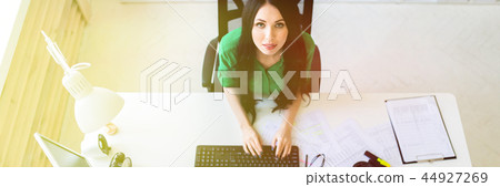 Top view of a young girl sitting at an office desk and typing on a keyboard. Top view of a young girl sitting at an office desk and typing on a keyboard. 44927269