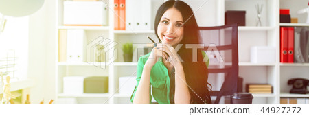 A young girl sits at the office table and holds a pencil in her hands. 44927272
