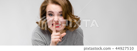 Charming young girl in a gray T-shirt on a gray background. The girl leaned her finger to her lips 44927510