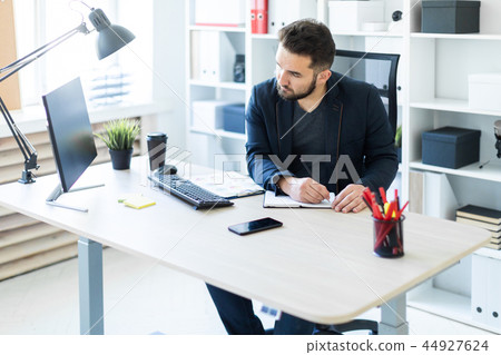 The young man works in the office at a computer Desk with documents, diagrams and phone. 44927624