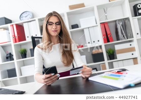 A young girl sitting at a table and holding a phone and a credit card. 44927741