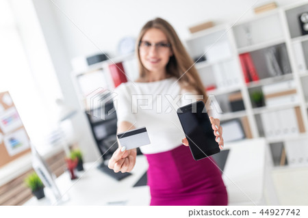 A young girl sitting at a table and holding a phone and a credit card. Photo with depth of field 44927742