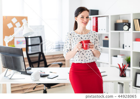 A young girl sat down on a computer Desk in the office and holding a red Cup. A young girl sat down on a computer Desk in the office and holding a red Cup. 44928065