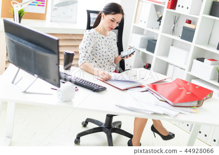 A young girl sitting in the office at the table, said on the calculator and working with documents. A young girl sitting in the office at the table, said on the calculator and working with documents. 44928066