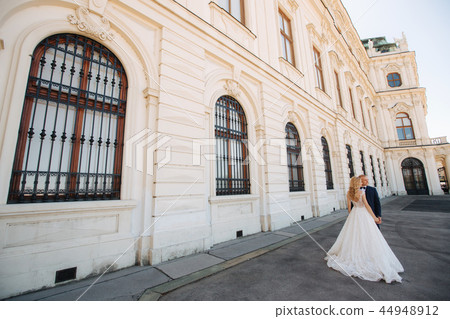 Couple walk near the big palace. Elegant groom and bride in their wedding clothes. Love 44948912