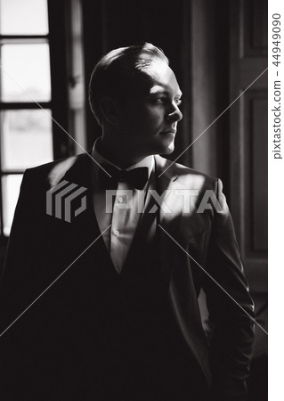 Handsome man in suit and tie bow stand near the window. Black and white picture 44949090