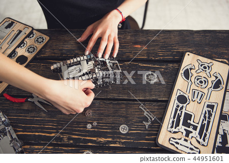 Careful woman sitting at the table and working with metal constructor 44951601