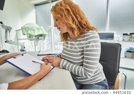 Beautiful red-haired lady looking at clipboard while having meeting with doctor Beautiful red-haired lady looking at clipboard while having meeting with doctor 44951638