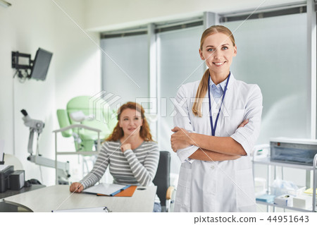 Young doctor standing with crossed arms while patient sitting at the table Young doctor standing with crossed arms while patient sitting at the table 44951643