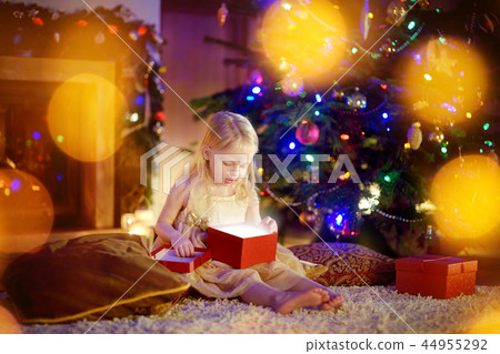 Happy girl opening Christmas gifts by a fireplace 44955292
