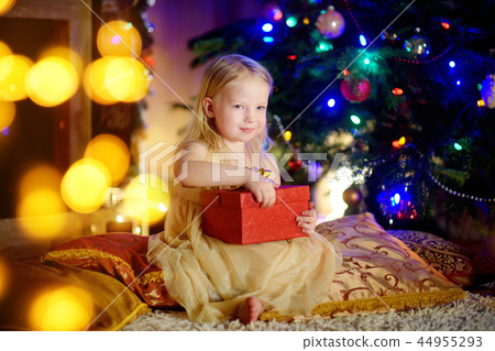 Happy girl opening Christmas gifts by a fireplace 44955293