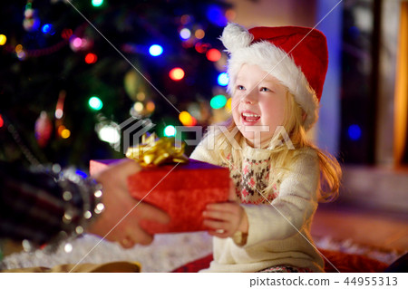 Happy little girl getting a Christmas gift from her parent Happy little girl getting a Christmas gift from her parent 44955313