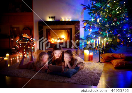 Mother and daughters using a tablet by a fireplace on Christmas 44955795