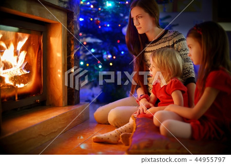 Young mother and daughters sitting by a fireplace on Christmas 44955797