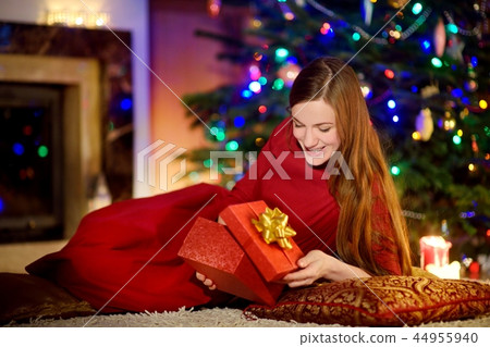 Beautiful woman enjoying her time by a fireplace on Christmas eve Beautiful woman enjoying her time by a fireplace on Christmas eve 44955940