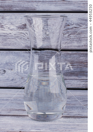 Clear glass vase with water on wooden background. Clear glass vase with water on wooden background. 44958250