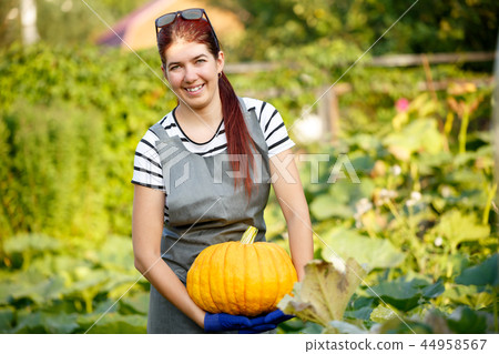 Portrait of happy woman with pumpkin in hands at garden 44958567