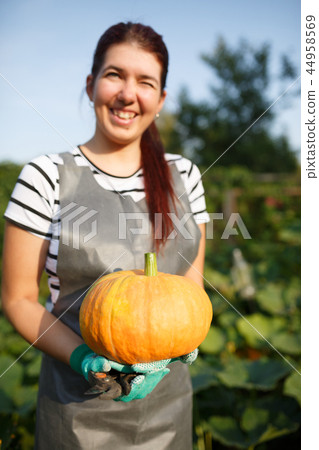 Photo of young woman with pumpkin in hands at garden on summer day Photo of young woman with pumpkin in hands at garden on summer day 44958569