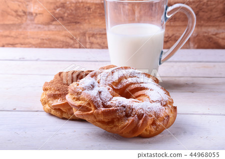 Chocolate and powdered sugar cream puff rings, choux pastry and glass with milk 44968055