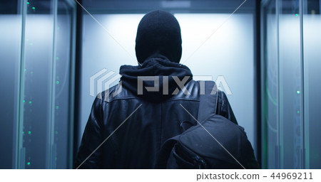 Hacker with a backpack walking through rows of rack servers 44969211