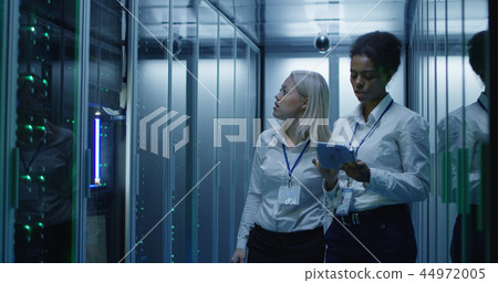 Two women are working in a data center with rows of server racks 44972005