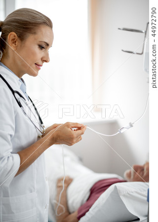 Doctor regulating IV infusion while patient resting on blurred background 44972790