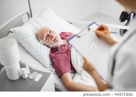 Smiling patient lying in bed near nightstand with medications Smiling patient lying in bed near nightstand with medications 44972886