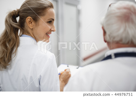 Smiling nurse looking at doctor while they walking in hospital hallway Smiling nurse looking at doctor while they walking in hospital hallway 44976751