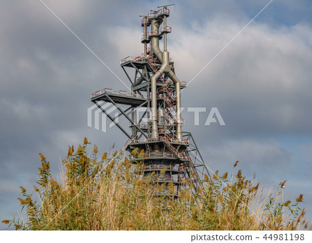 Old blast furnace behind bush and cloudy sky 44981198