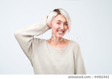 Puzzled woman with dyed short hair wearing gray sweater looking into camera having some doubts 44982891