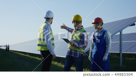 Workers talking inbetween long rows of solar panels Workers talking inbetween long rows of solar panels 44983304