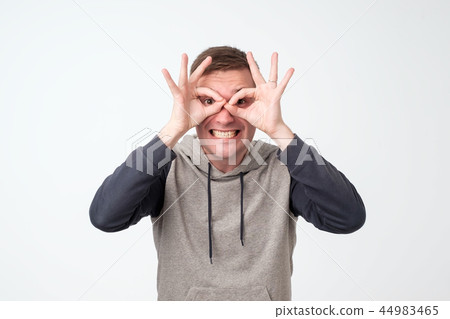 Young man showing owl sign with fingers. Making funny grimace 44983465
