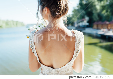 View of unrecognazible young woman in wedding dress standing by back and looking away. 44986329