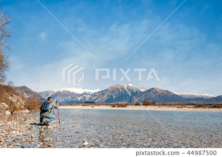 Mature hiker on the bank of a river. Mature hiker on the bank of a river. 44987500