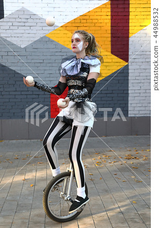 Girl clown rides a unicycle and juggles balls Girl clown rides a unicycle and juggles balls 44988532