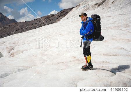 Traveler in a cap and sunglasses with a backpack on his shoulders in the snowy mountains on the Traveler in a cap and sunglasses with a backpack on his shoulders in the snowy mountains on the 44989302