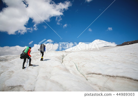 Two tourists, a man and a woman with backpacks and crampons on their feet walk along the glacier Two tourists, a man and a woman with backpacks and crampons on their feet walk along the glacier 44989303