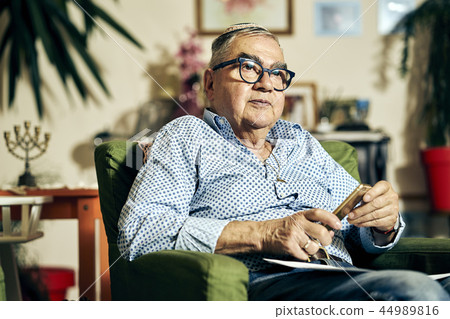 Pensive Jewish senior in the armchair reading a torah book Pensive Jewish senior in the armchair reading a torah book 44989816