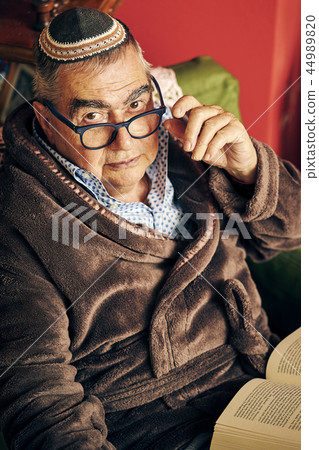 Jewish senior with glasses in the armchair reading a torah book Jewish senior with glasses in the armchair reading a torah book 44989820