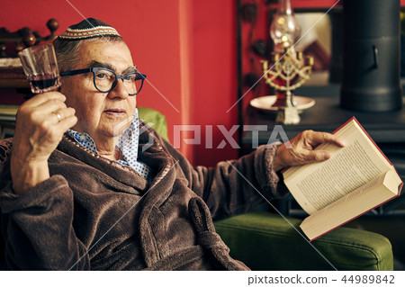 Pensive Jewish senior reading a torah book and drinking kosher wine Pensive Jewish senior reading a torah book and drinking kosher wine 44989842